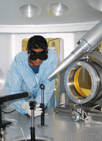 Person in light blue lab coat setting equipment in front of laser.